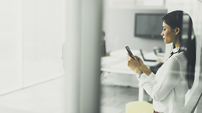 Woman in business attire standing in an office while using a smart phone