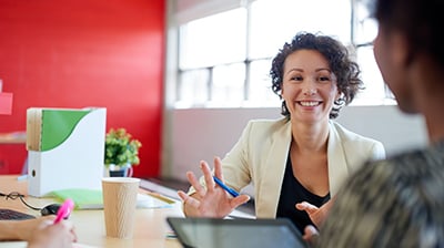 Woman dressed in business casual attire sitting with colleagues smiling.