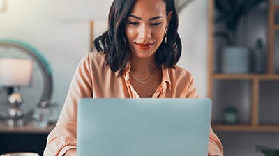 Woman working on laptop online, checking emails and planning on the internet while sitting in an office alone at work.