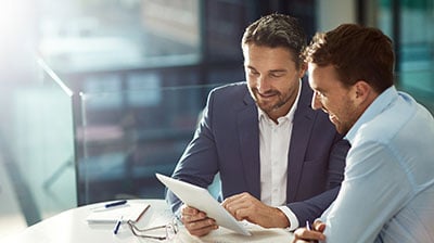 Two businessmen using a tablet while sitting at a table 