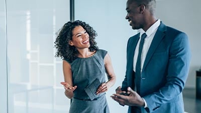 A man and a woman dressed in business attire, standing next to each other while having a discussion 