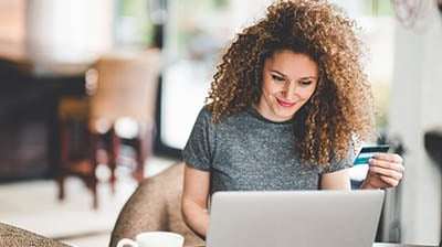 Woman holding credit card shopping online on a laptop.