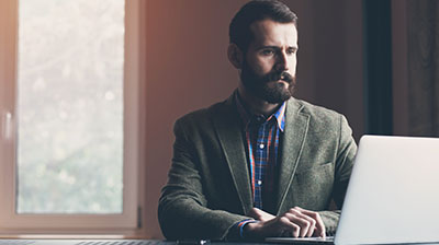 Man in business attire sitting at a table with a laptop open in front of him.