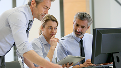 Two businessmen and a business woman working together on a computer and a tablet