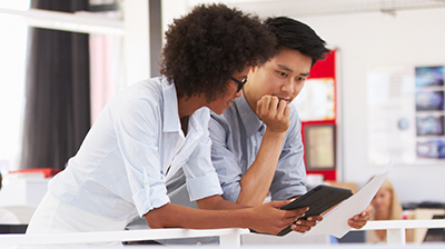 Two coworkers comparing notes on a tablet