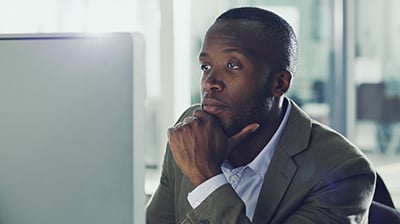 Man dressed in business casual attire looking at computer screen with his chin resting in his hand.