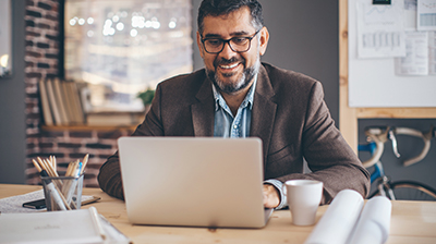 A man sitting at a desk, smiling while using his laptop 