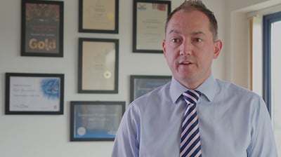 A man in a tie standing in front of a number of awards