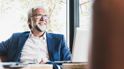 Man in business attire sitting behind a desk in an office while looking forward.