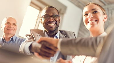 Colleagues dressed in business attire conversing and two of them shake hands.