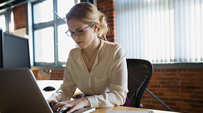 Woman in business attire sitting at desk using a laptop. 